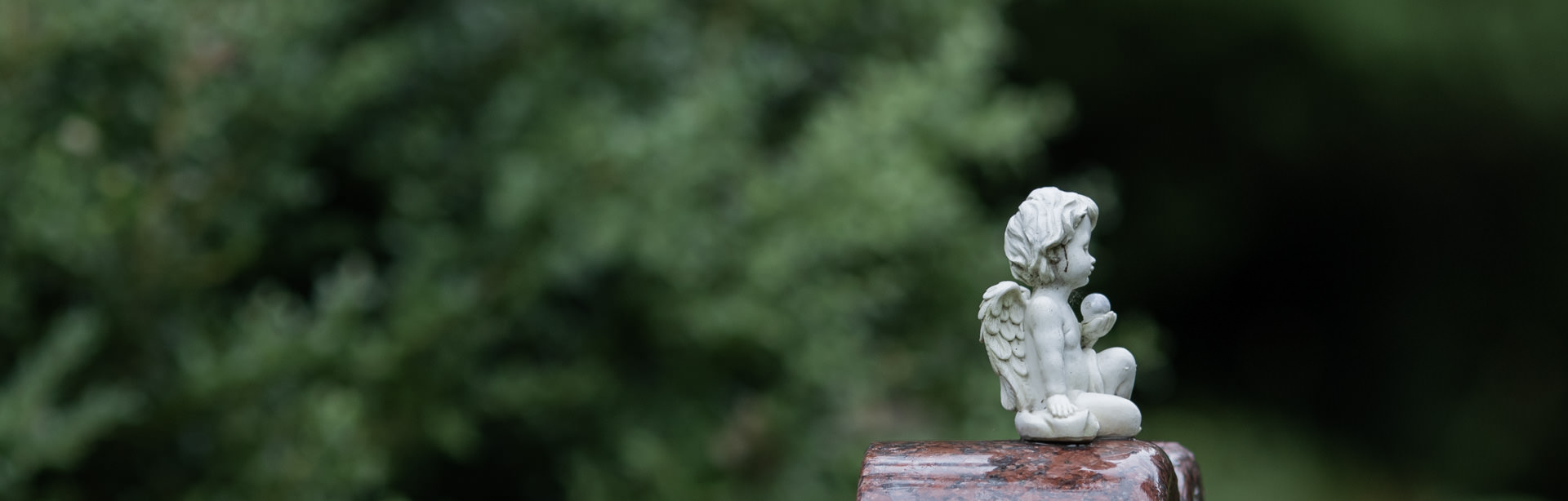 Engelsfigur sitzt auf einem Grabstein